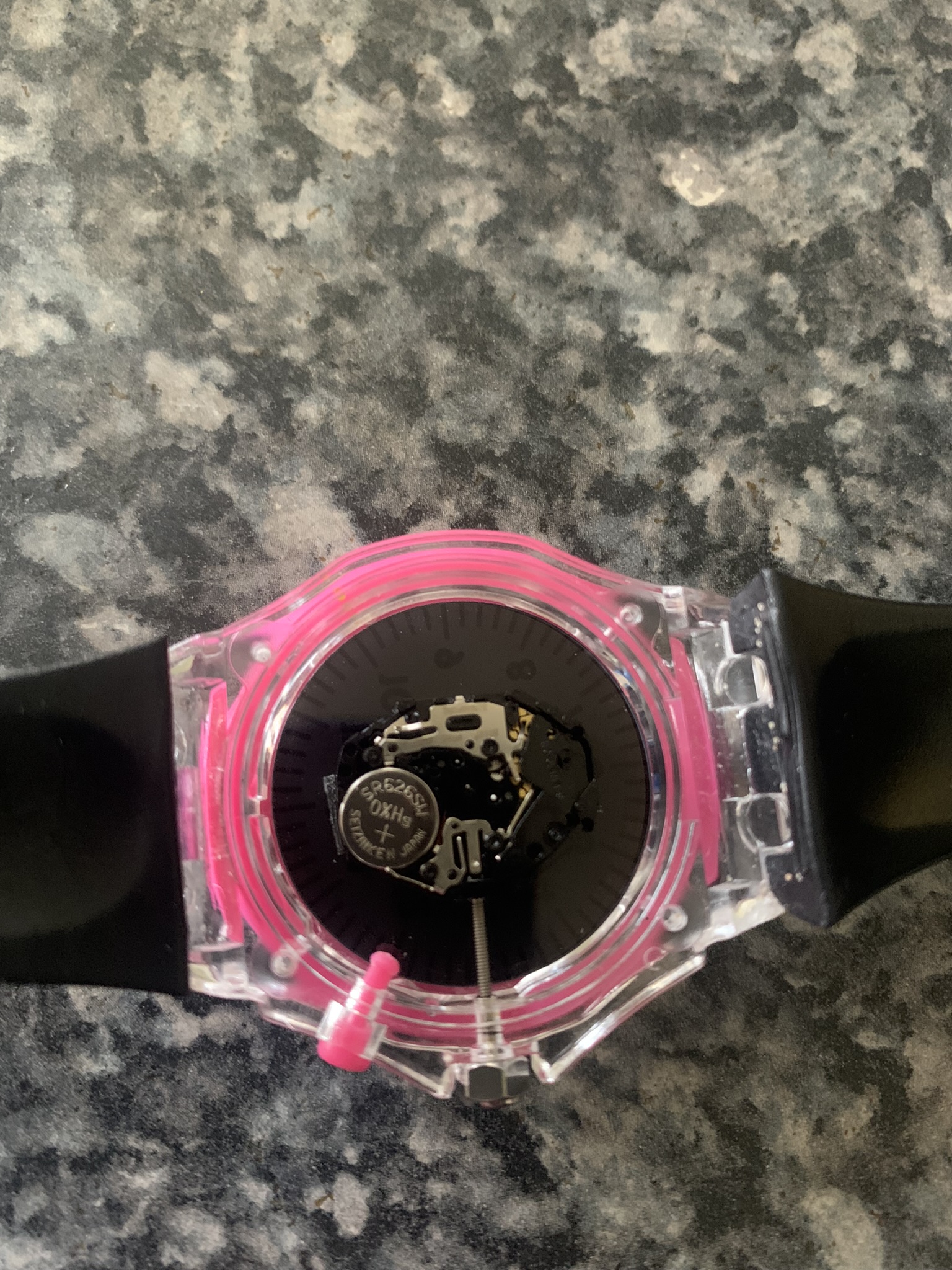 A child's watch with an opened back exposing the inner mechanism. The primary colour is pink, the primary mode of operation is 'broken'.